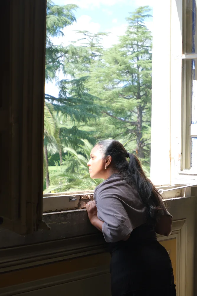A woman looking through an open window toward a green garden