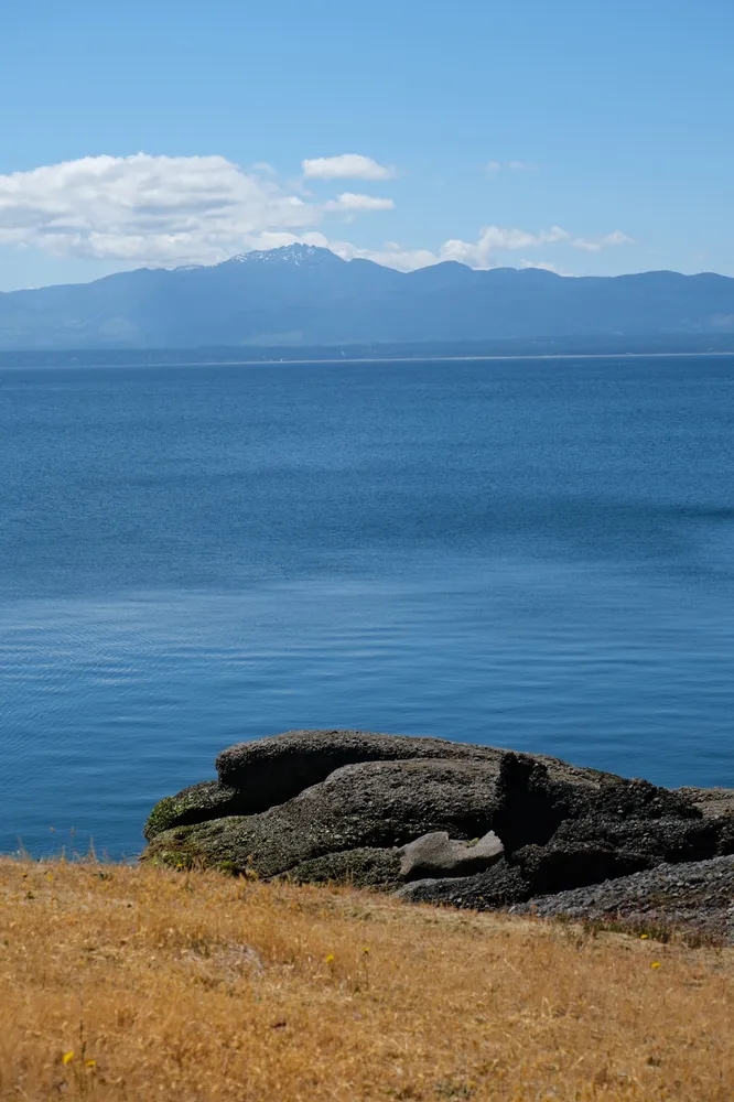 Blue coastal water, rocky shoreline, and distant mountains