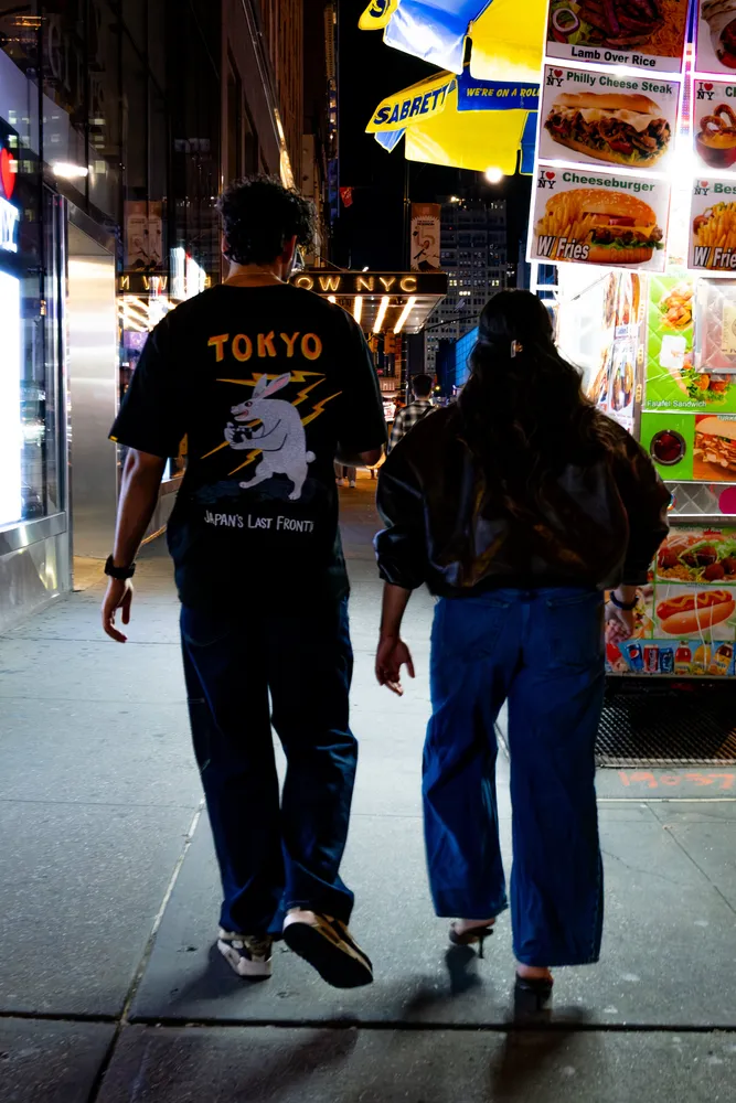 Two people walking past brightly lit storefronts at night